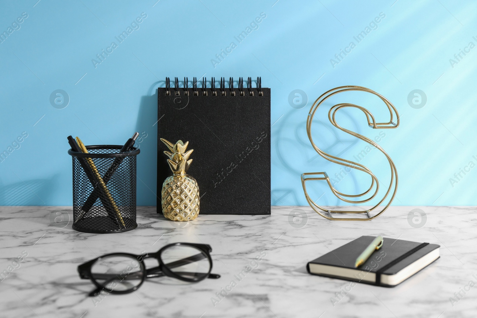 Photo of Stylish office workplace. Decor elements, glasses and stationery on white table near light blue wall