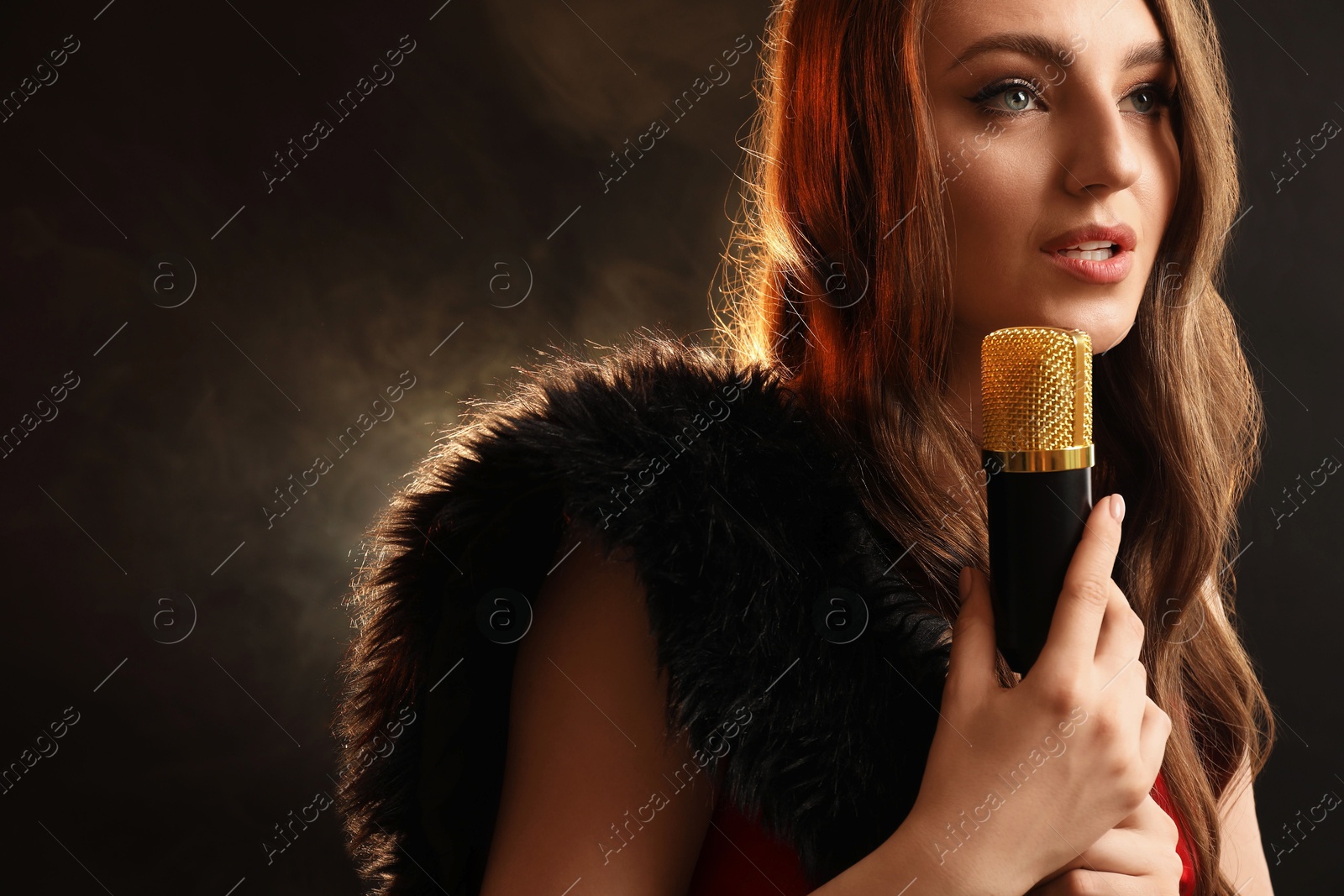 Photo of Beautiful young jazz singer with microphone on dark background with smoke. Space for text