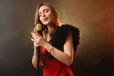 Photo of Beautiful young woman in stylish dress with microphone singing on dark background in color lights and smoke