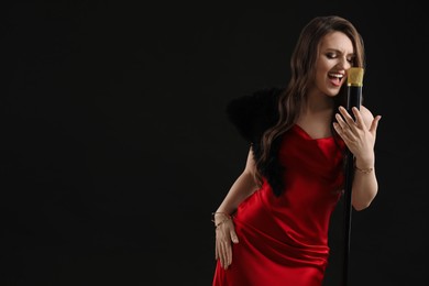 Photo of Beautiful young woman in stylish dress with microphone singing on black background, space for text