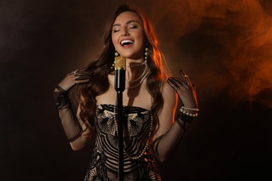 Photo of Beautiful young woman with microphone singing in color lights and smoke