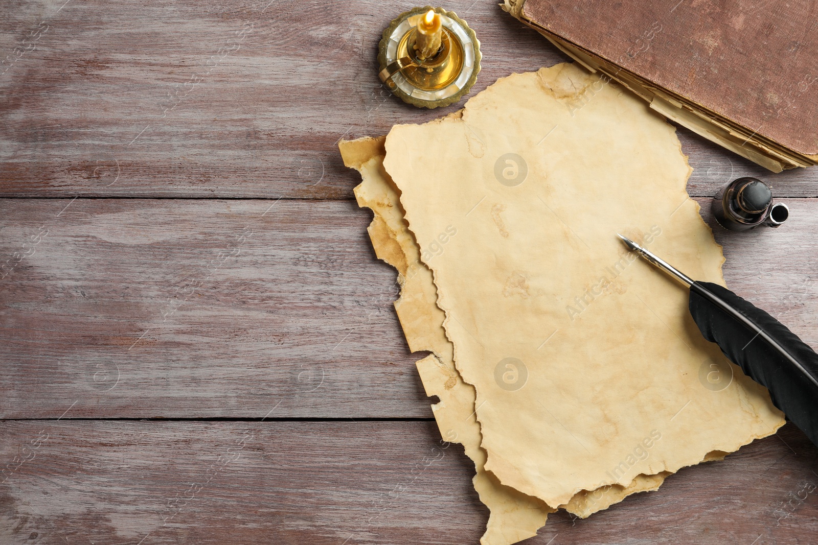 Photo of Sheet of old parchment paper, black feather, inkwell, vintage book and candle on wooden table, flat lay. Space for text