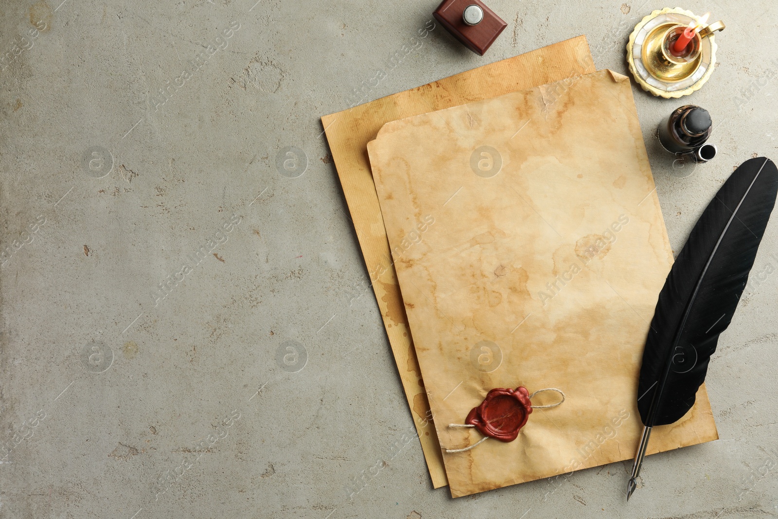 Photo of Sheet of old parchment paper with wax stamp, black feather, inkwell and candle on grey table, flat lay. Space for text