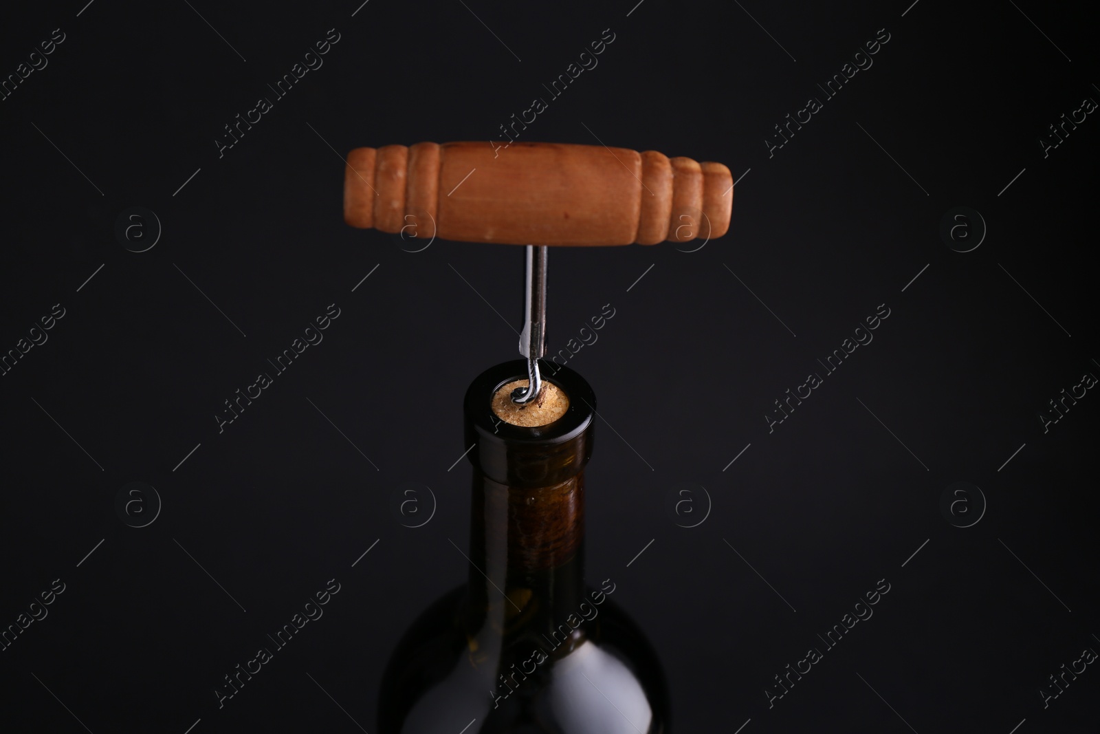 Photo of Wine bottle with corkscrew on dark background, closeup