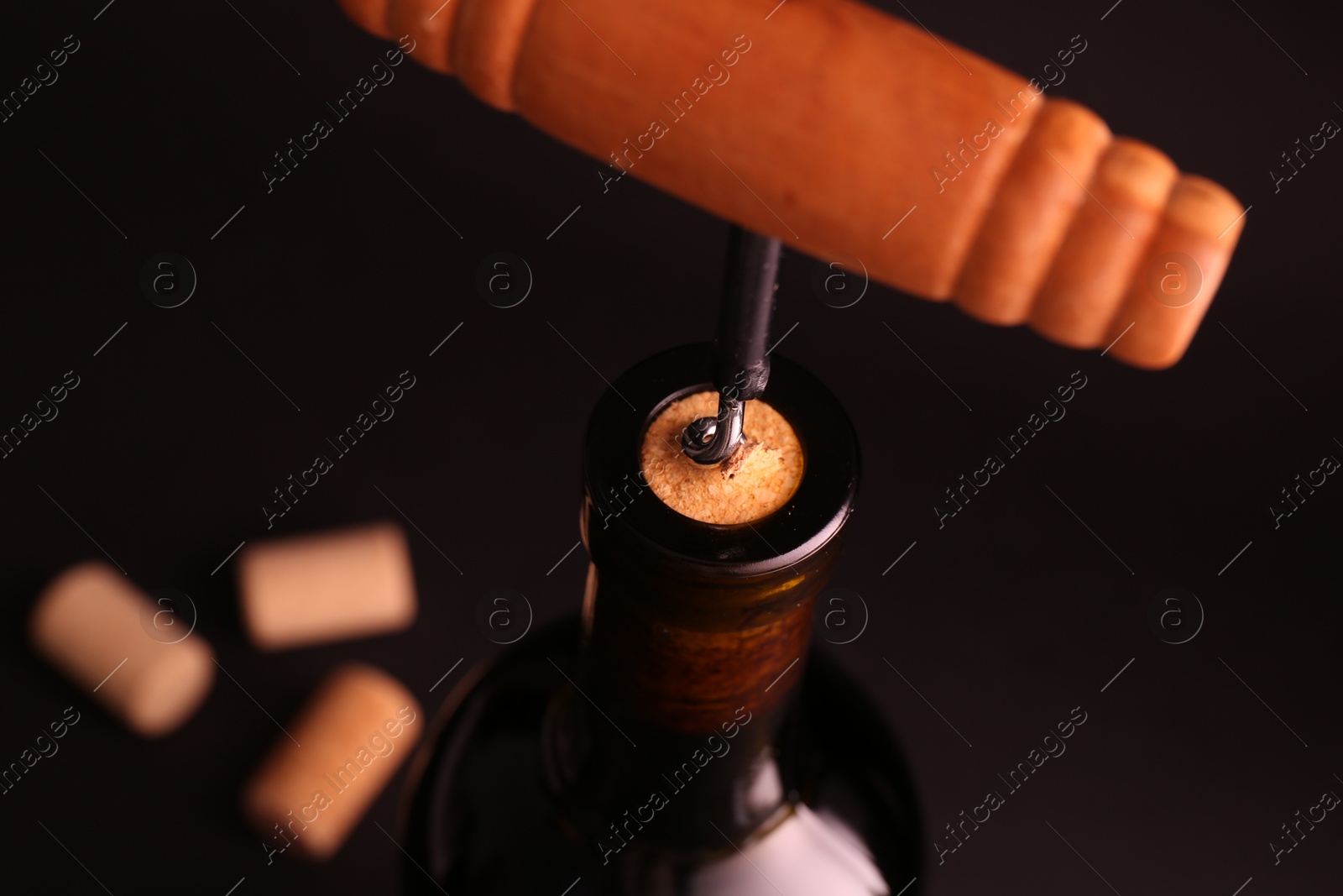 Photo of Wine bottle with corkscrew on dark background, closeup