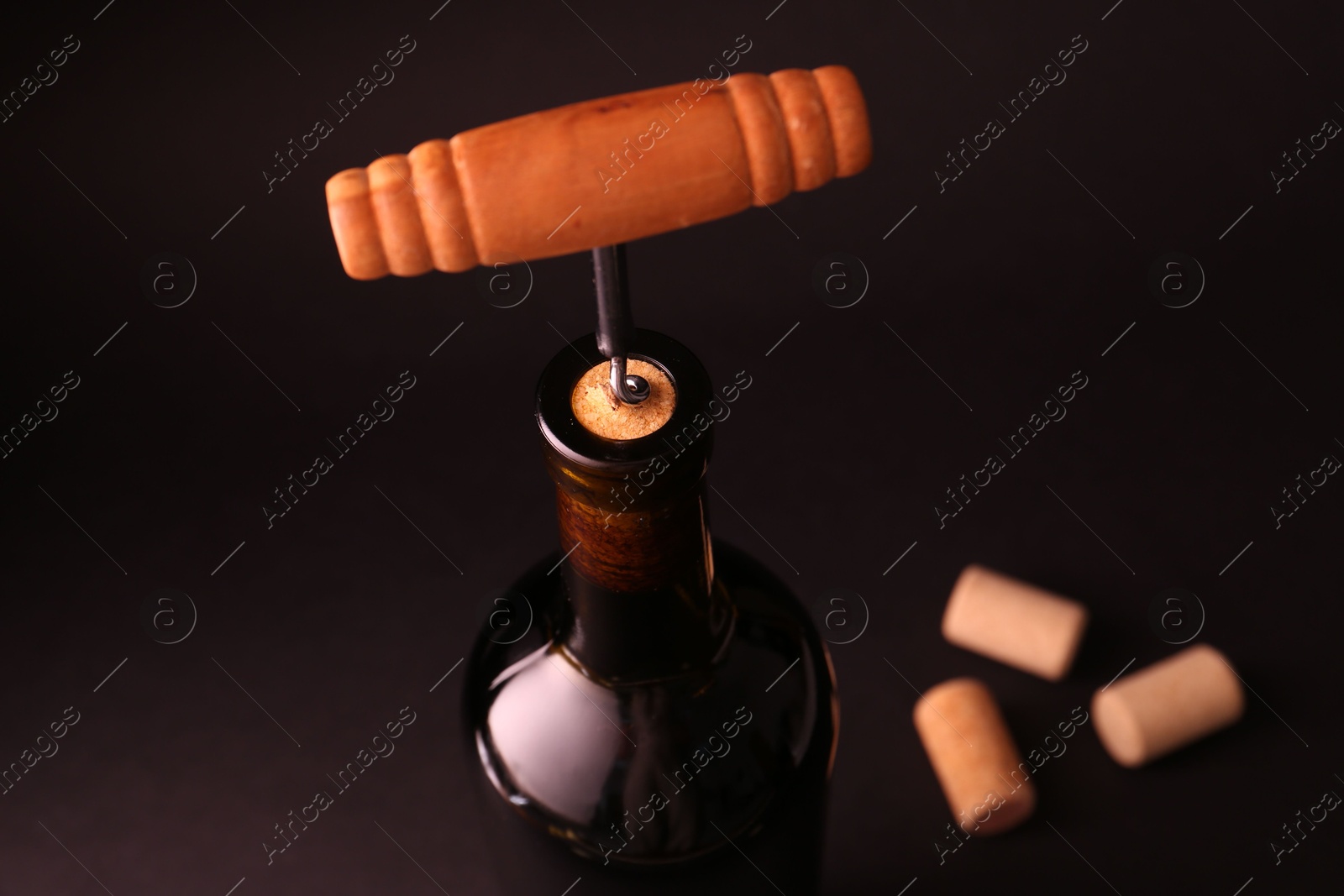 Photo of Wine bottle with corkscrew on dark background, closeup