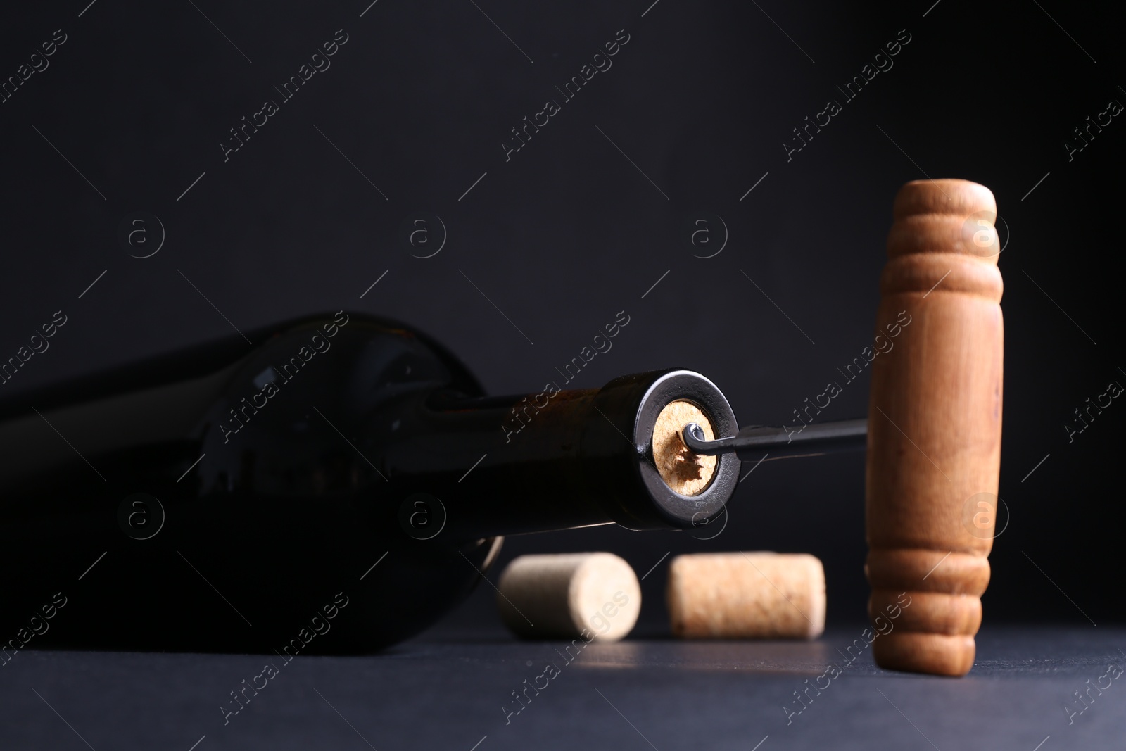 Photo of Wine bottle with corkscrew on dark background, closeup