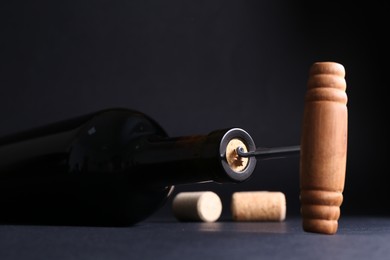 Photo of Wine bottle with corkscrew on dark background, closeup