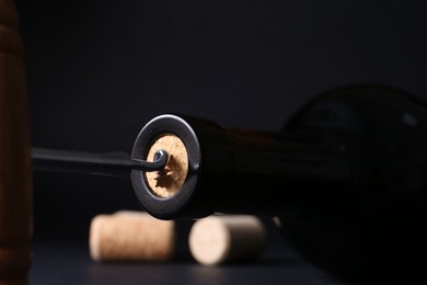 Wine bottle with corkscrew on dark background, closeup