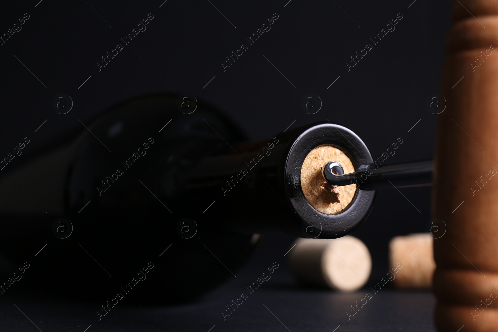 Photo of Wine bottle with corkscrew on dark background, closeup