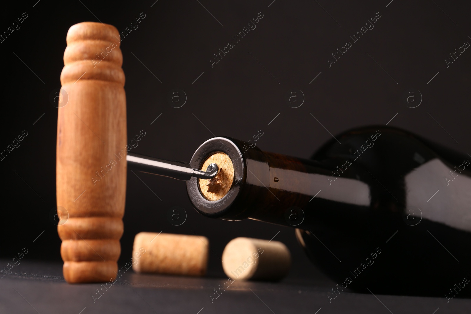 Photo of Wine bottle with corkscrew on dark background, closeup