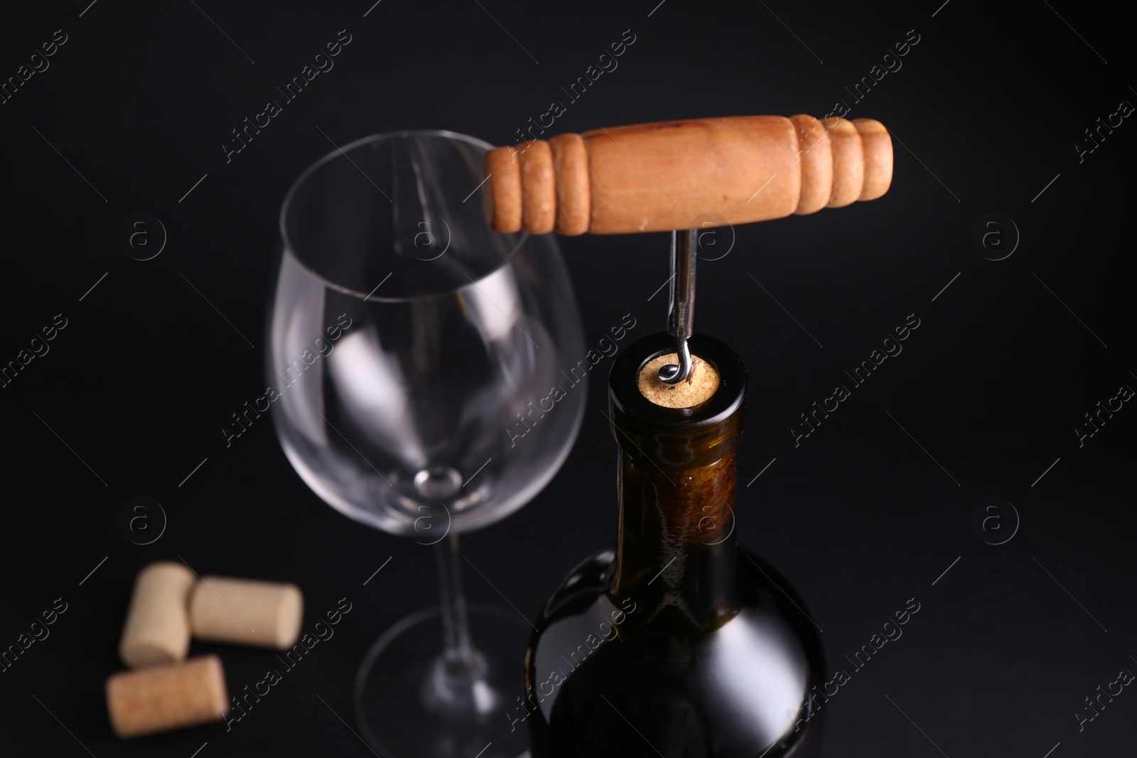 Photo of Wine bottle with corkscrew on dark background, closeup