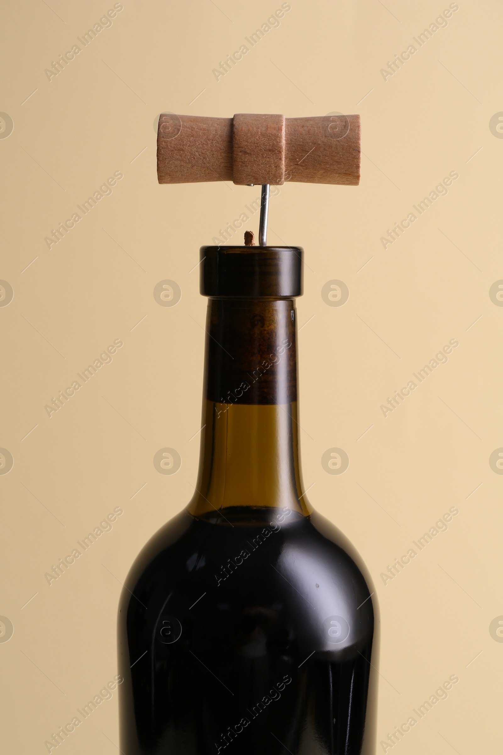 Photo of Wine bottle with corkscrew on beige background, closeup