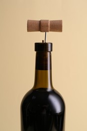 Wine bottle with corkscrew on beige background, closeup