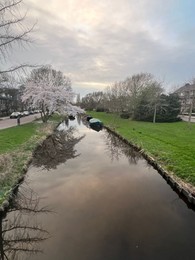 Photo of Picturesque view of canal with moored boats and blossoming trees in spring