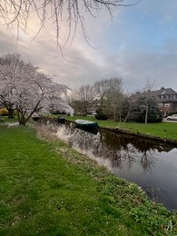 Photo of Picturesque view of canal with moored boats and blossoming trees in spring