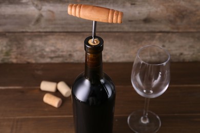 Wine bottle with corkscrew and glass on wooden table