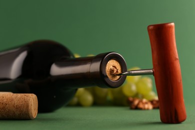 Photo of Wine bottle with corkscrew on green background, closeup