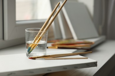 Brushes, glass of water and blank canvases on window sill, closeup