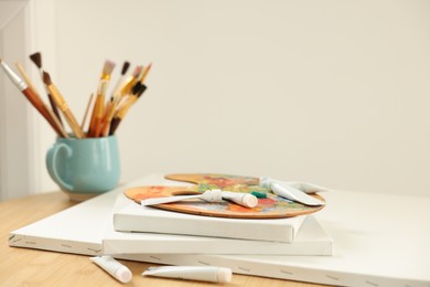 Photo of Artist's palette, paints and blank canvases on wooden table indoors, closeup