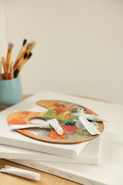 Artist's palette, paints and blank canvases on wooden table indoors, closeup