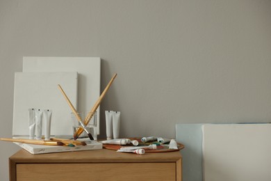 Photo of Artist's palette, brushes, canvases and paints on wooden chest of drawers indoors. Space for text