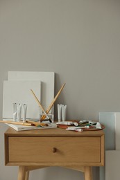 Photo of Artist's palette, brushes in glass of water, blank canvases and paints on wooden table indoors