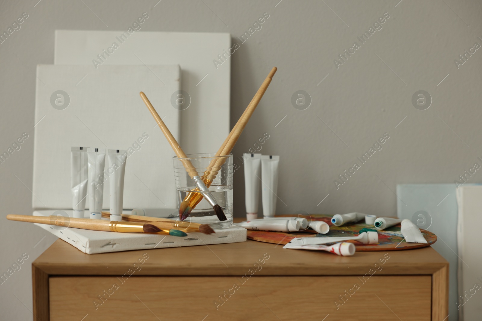 Photo of Artist's palette, brushes, canvases and paints on wooden chest of drawers indoors