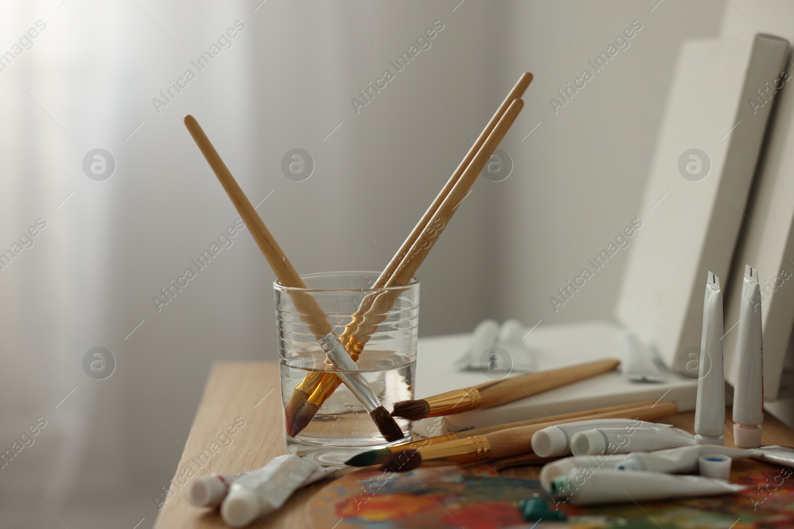 Photo of Artist's palette, brushes in glass of water and paints on wooden table indoors