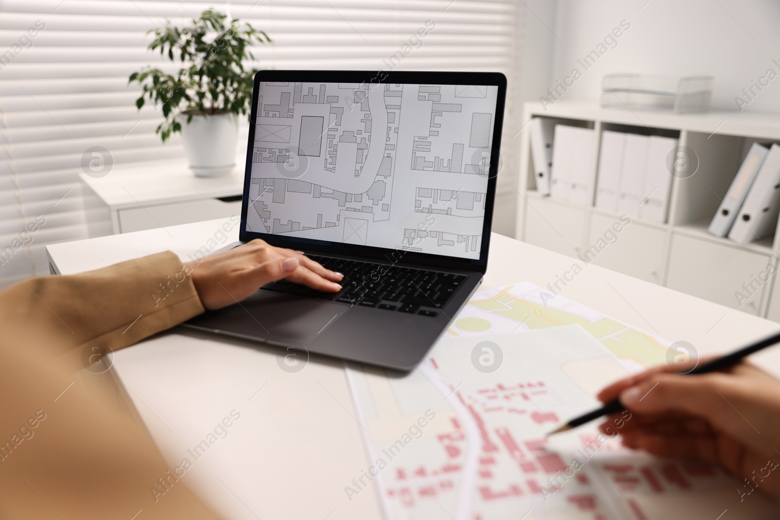 Photo of Cartographer working with cadastral map on laptop at white table in office, closeup