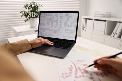 Cartographer working with cadastral map on laptop at white table in office, closeup