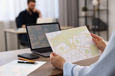Cartographer working with cadastral maps at wooden table in office, closeup