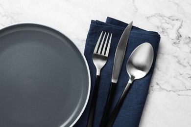 Stylish cutlery, napkin and plate on white marble table, top view