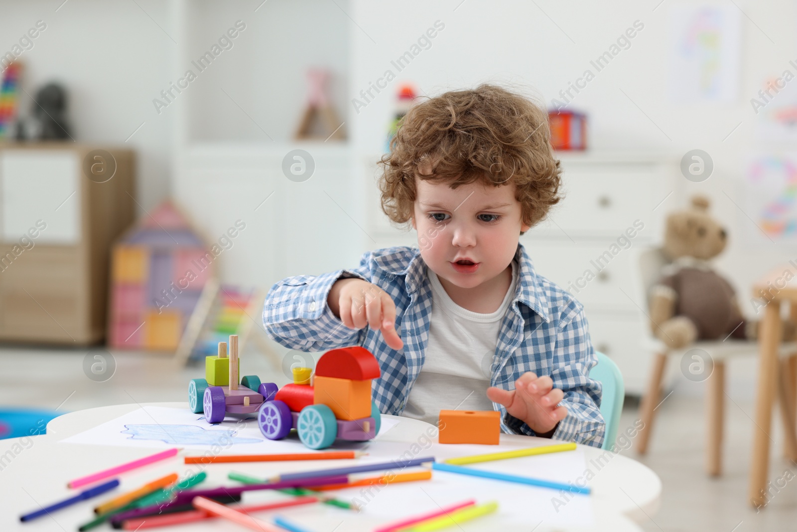 Photo of Cute little boy playing with toy cars at white table in kindergarten