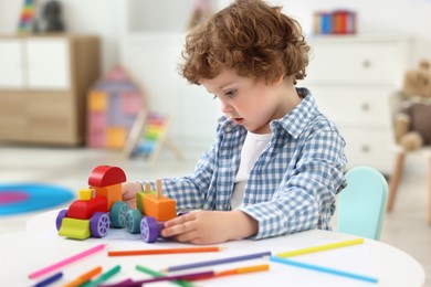 Cute little boy playing with toy cars at white table in kindergarten