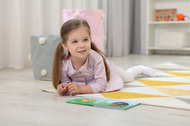 Photo of Cute little girl with book on floor in kindergarten