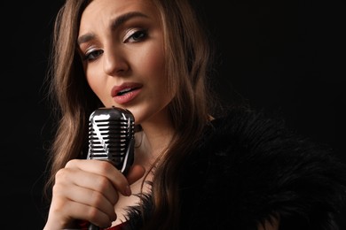 Photo of Beautiful young woman with microphone singing on black background