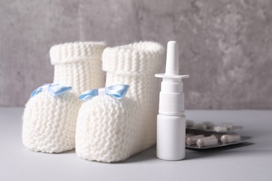 Photo of Baby`s booties, nasal spray and pills on grey table, closeup