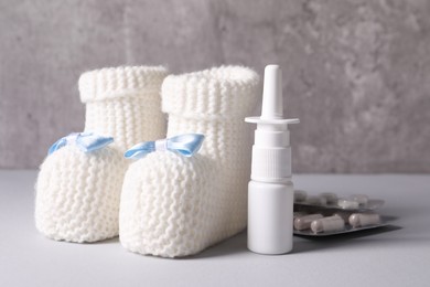 Baby`s booties, nasal spray and pills on grey table, closeup