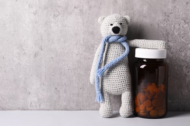 Photo of Toy bear and bottle of pills on light table near grey wall, space for text