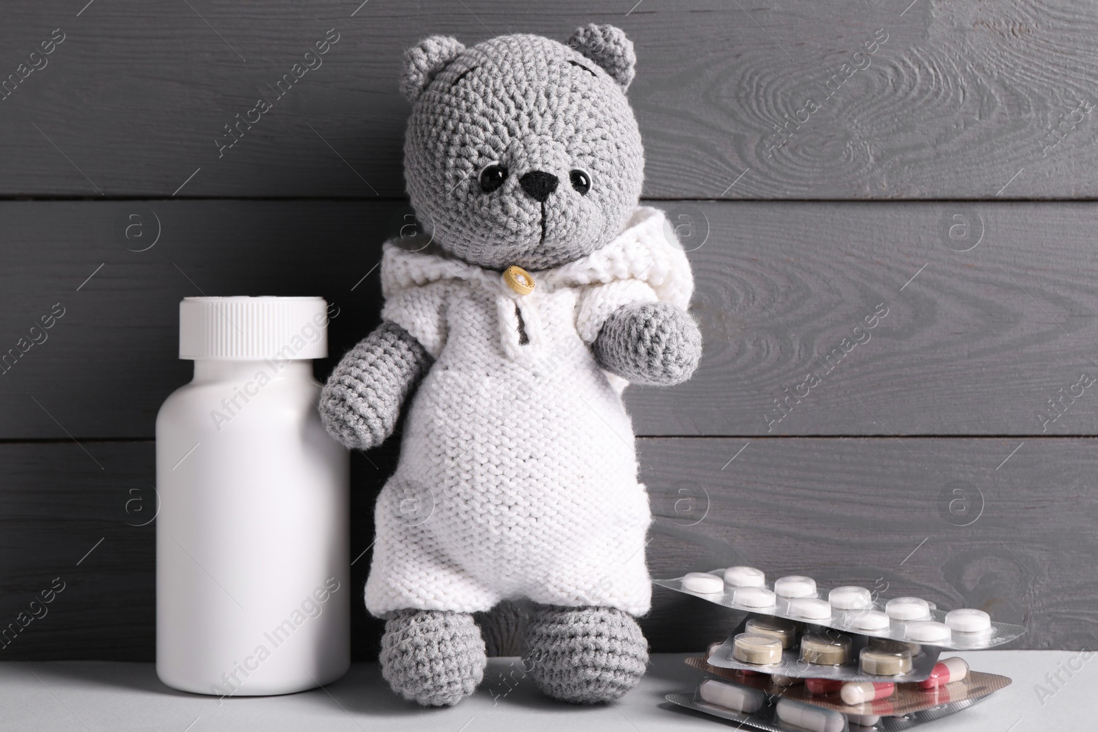 Photo of Toy bear with pills on light table near grey wooden wall