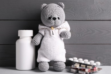 Toy bear with pills on light table near grey wooden wall