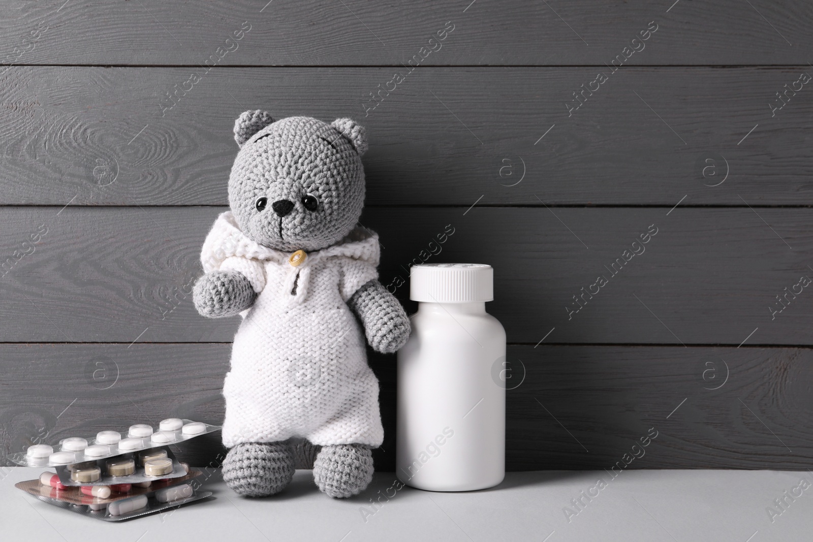 Photo of Toy bear with pills on light table near grey wooden wall, space for text