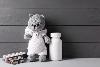 Toy bear with pills on light table near grey wooden wall, space for text