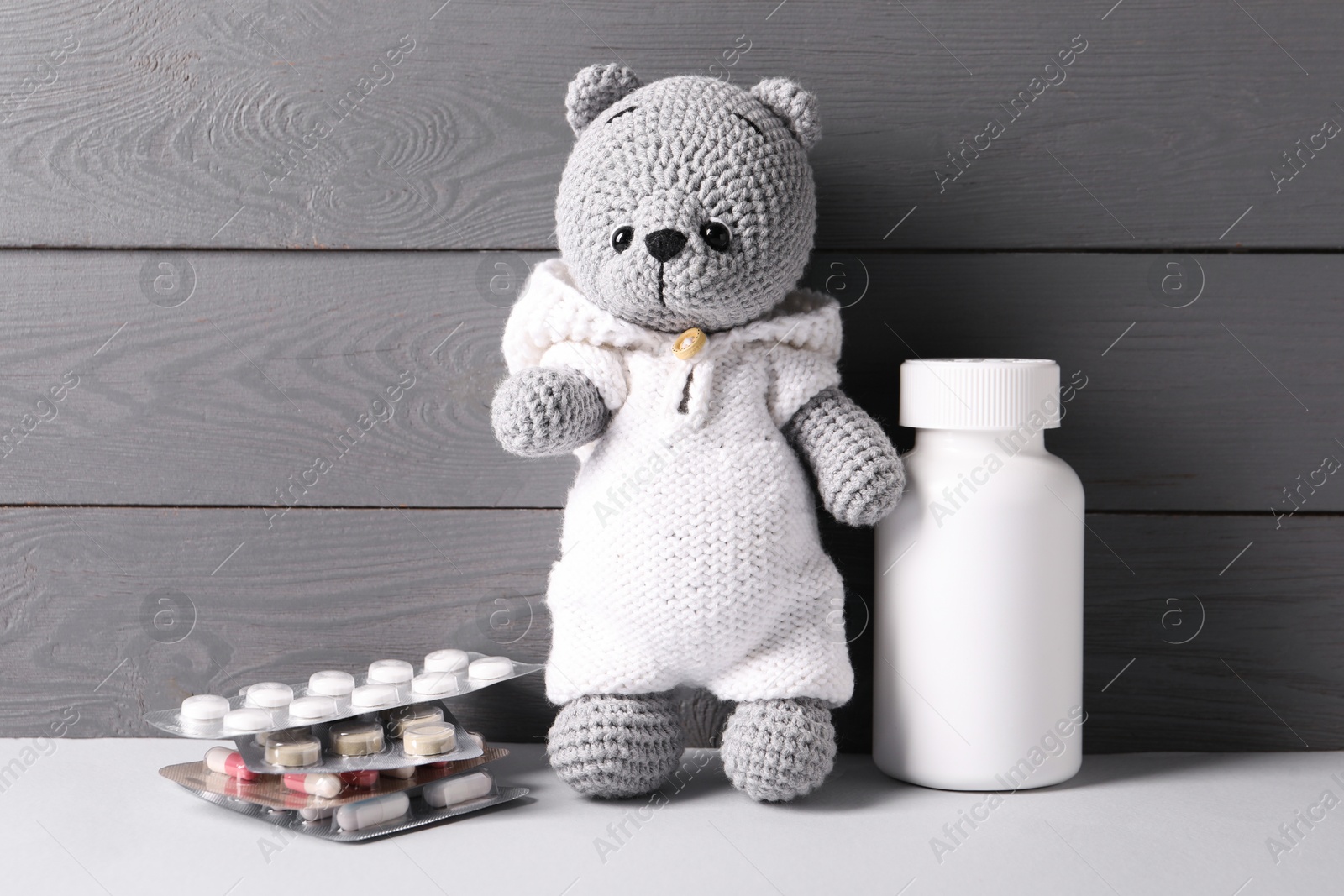 Photo of Toy bear with pills on light table near grey wooden wall