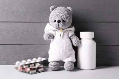 Toy bear with pills on light table near grey wooden wall