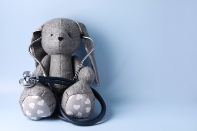 Toy bunny with stethoscope on light blue background, space for text