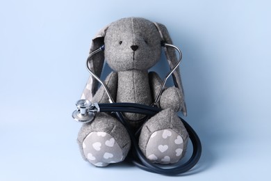 Toy bunny with stethoscope on light blue background