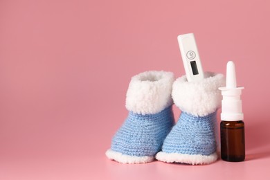 Photo of Baby`s booties, thermometer and nasal spray on pink background, space for text