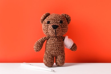 Photo of Toy bear with bandage and thermometer on color background